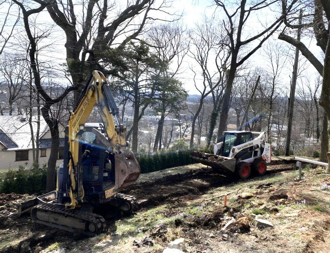 Excavator and skid steer clearing wooded hillside lot