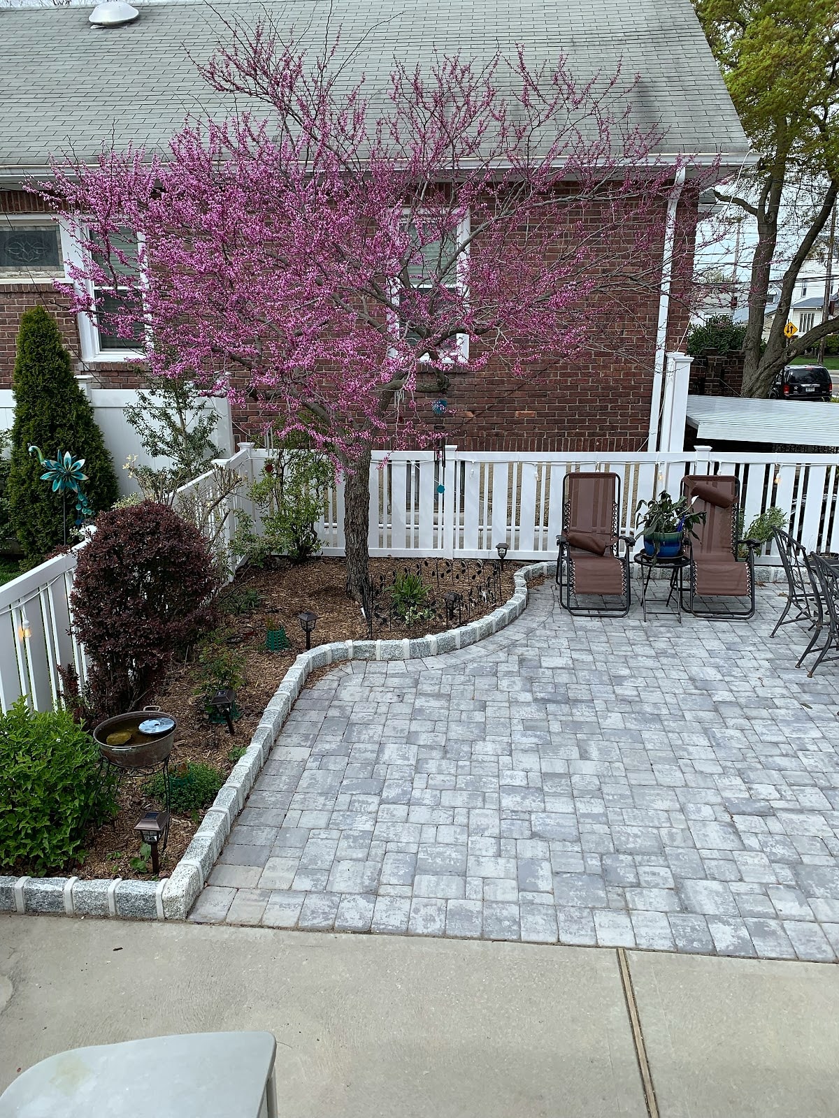 Gray paver patio with curved garden border, flowering tree and lounge chairs